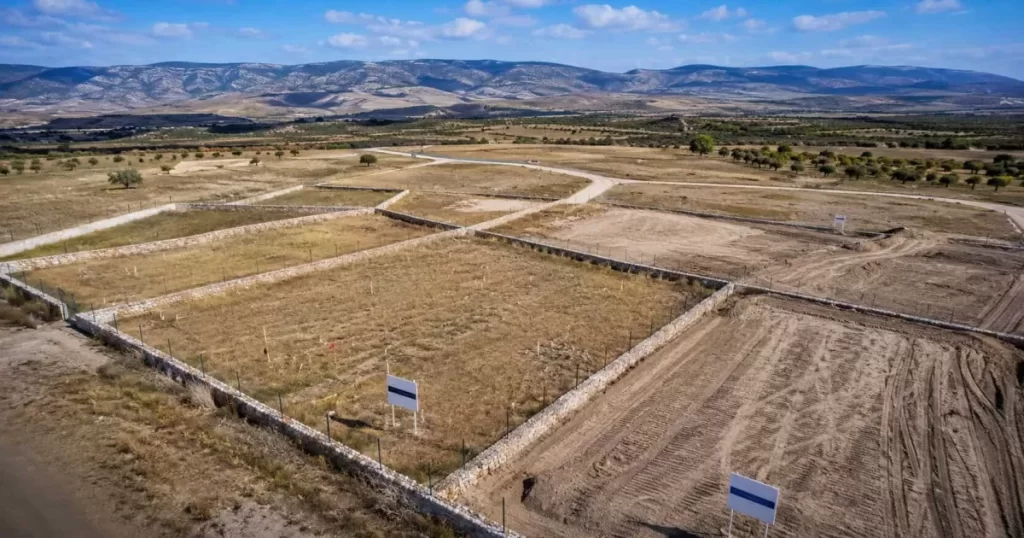 Vista aérea drone de parcelas residenciales urbanizables en las afueras de Zaragoza con linderos delimitados, terrenos de tierra ocre, vegetación seca del Valle del Ebro y montañas pedreras al fondo