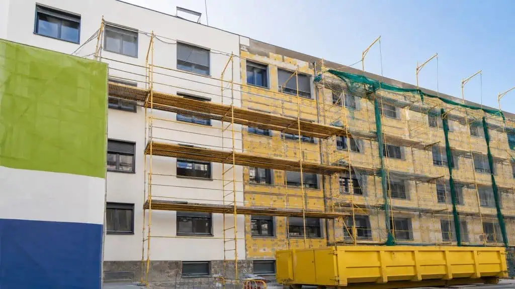 Bloque de viviendas años 70-80 en Zaragoza durante rehabilitación energética con sistema SATE parcialmente instalado, paneles de XPS amarillo, ventanas de aluminio con rotura puente térmico y andamios metálicos