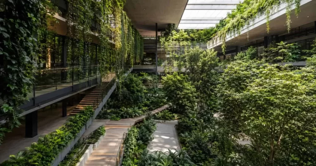 Atrio biofílico de un edificio moderno con árboles, jardines verticales y luz cenital, arquitectura que conecta con la naturaleza 2026
