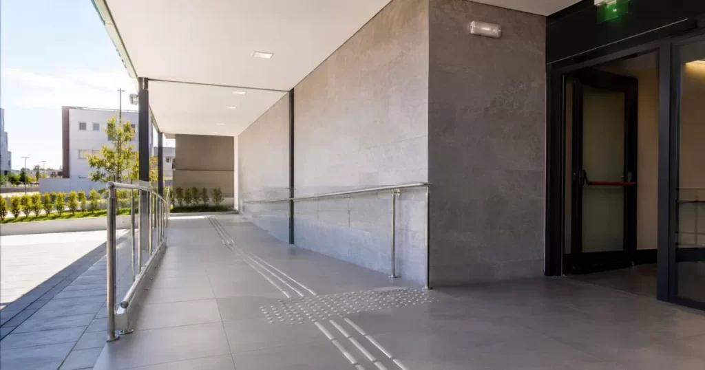 Acceso de un edificio con rampa accesible, pavimento podotáctil y salida de emergencia, cumplimiento del CTE y normativa española